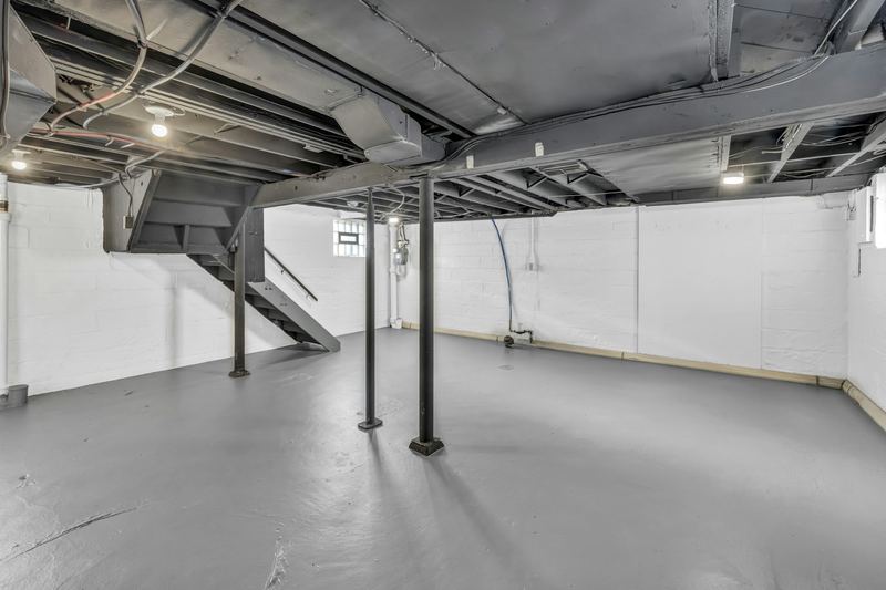 Spacious unfinished basement with exposed joists, support poles and stairs